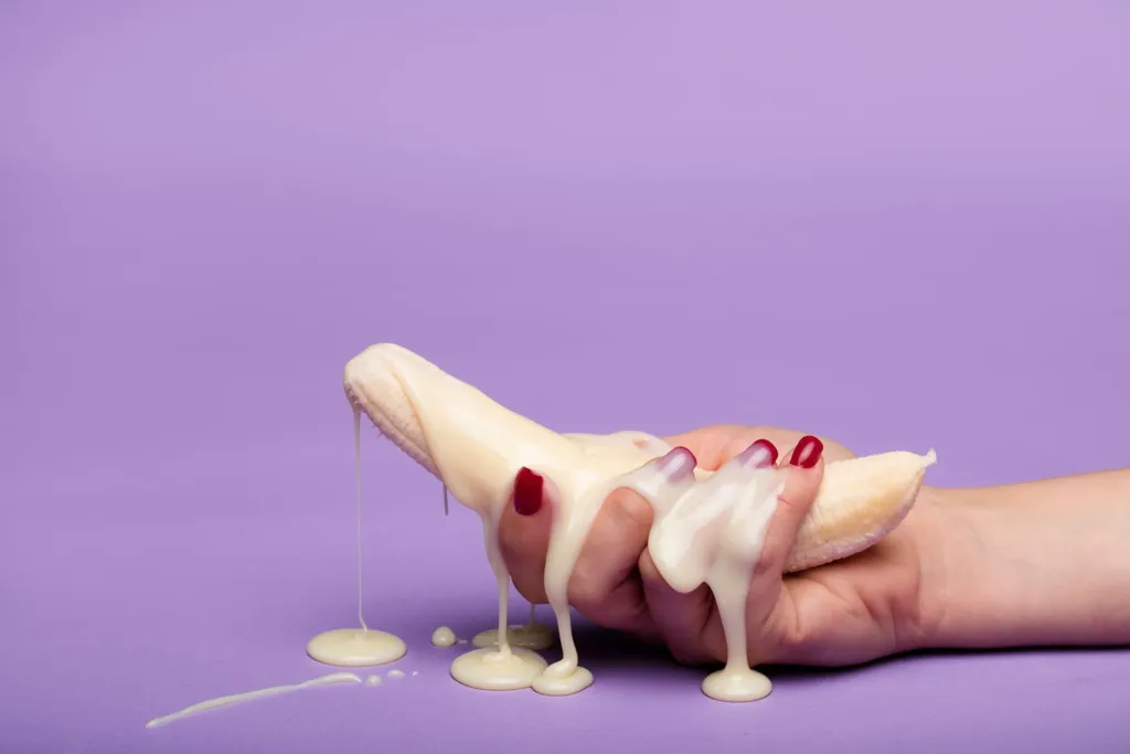Creative conceptual image of a banana with cream on a purple backdrop, symbolizing indulgence.